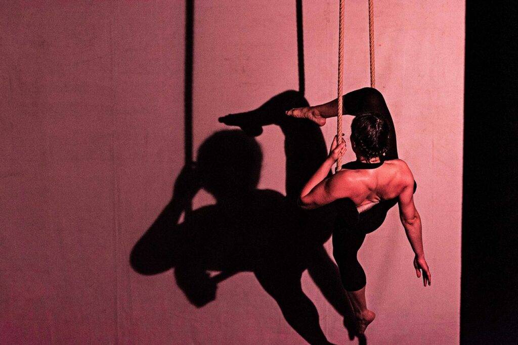 Artista appeso a un trapezio, si vede la sua ombra su un telo chiaro