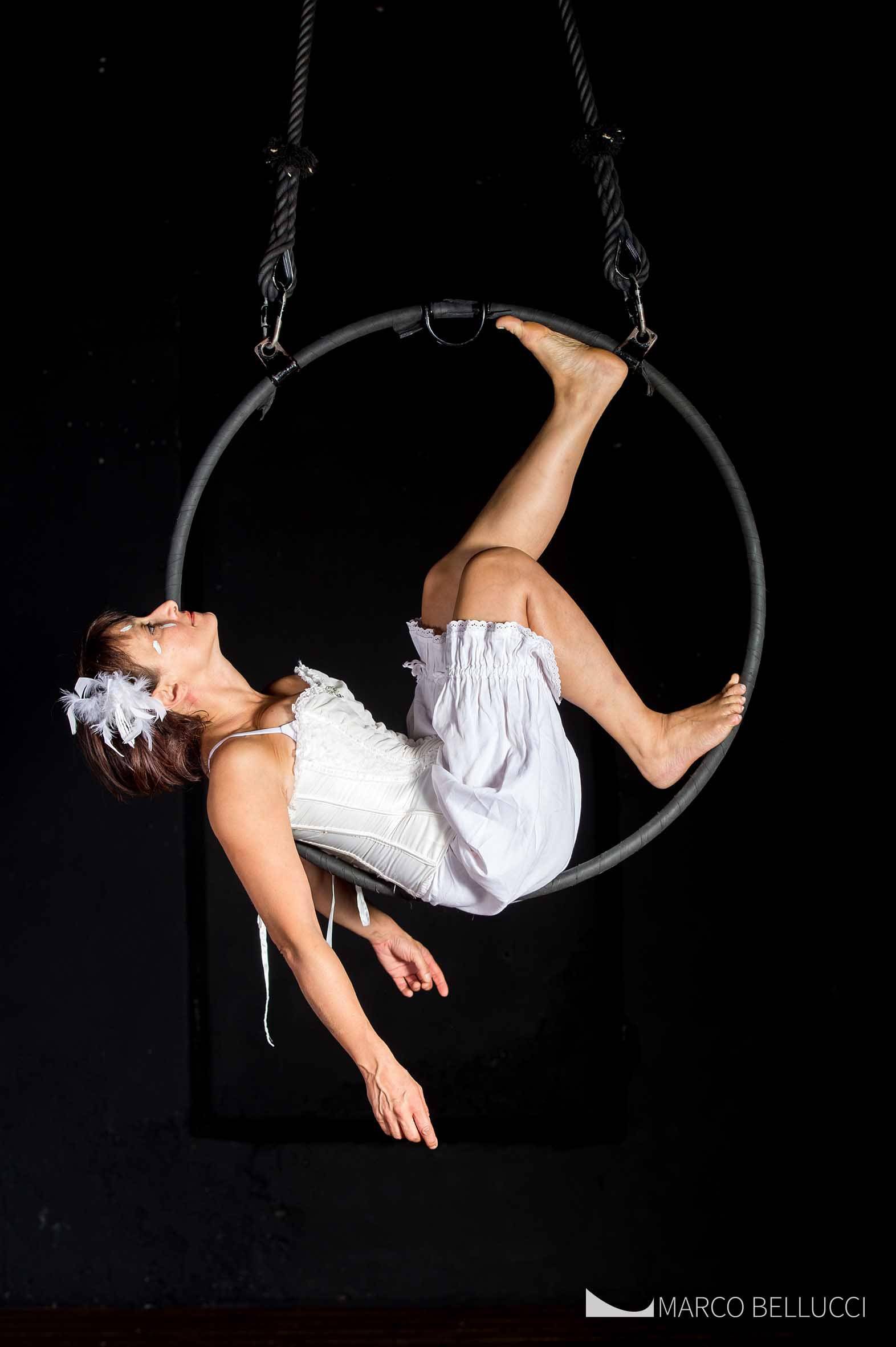 Una donna in abito bianco appesa su un grande anello nero