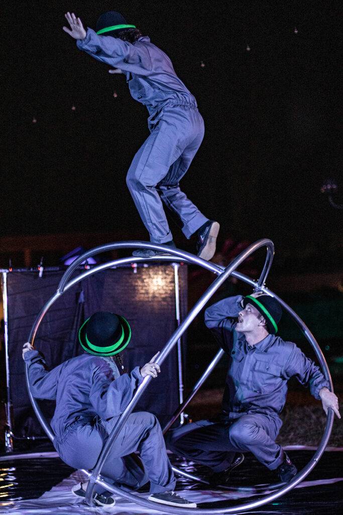 Un gruppo di uomini che si esibisce sul palco Uno cammina sopra un grande giroscopio di metallo